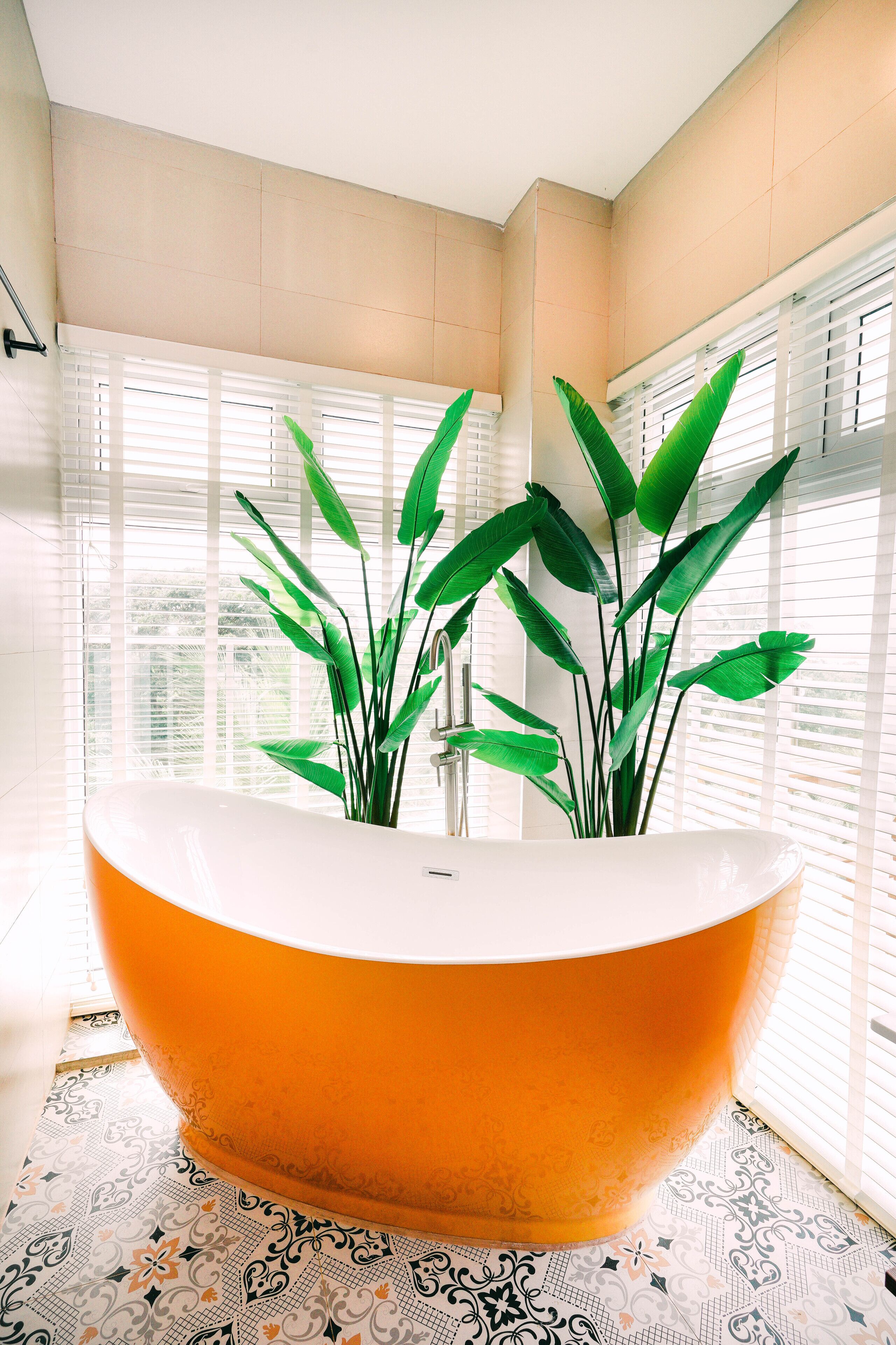 A bathroom with a freestanding bathtub, large windows with blinds, and a patterned floor.