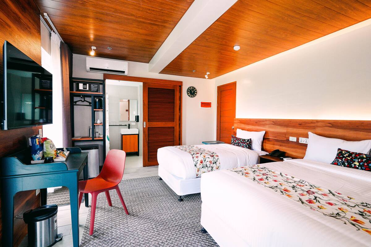 Une chambre d’hôtel avec un plafond en bois, un bureau avec une chaise, un lit avec une literie à motifs floraux et une table de chevet.