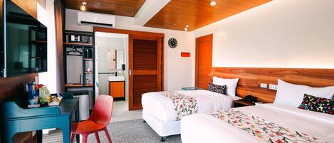 Habitación de hotel con techo de madera, un escritorio con silla, cama con ropa de cama floral y una mesita de noche.