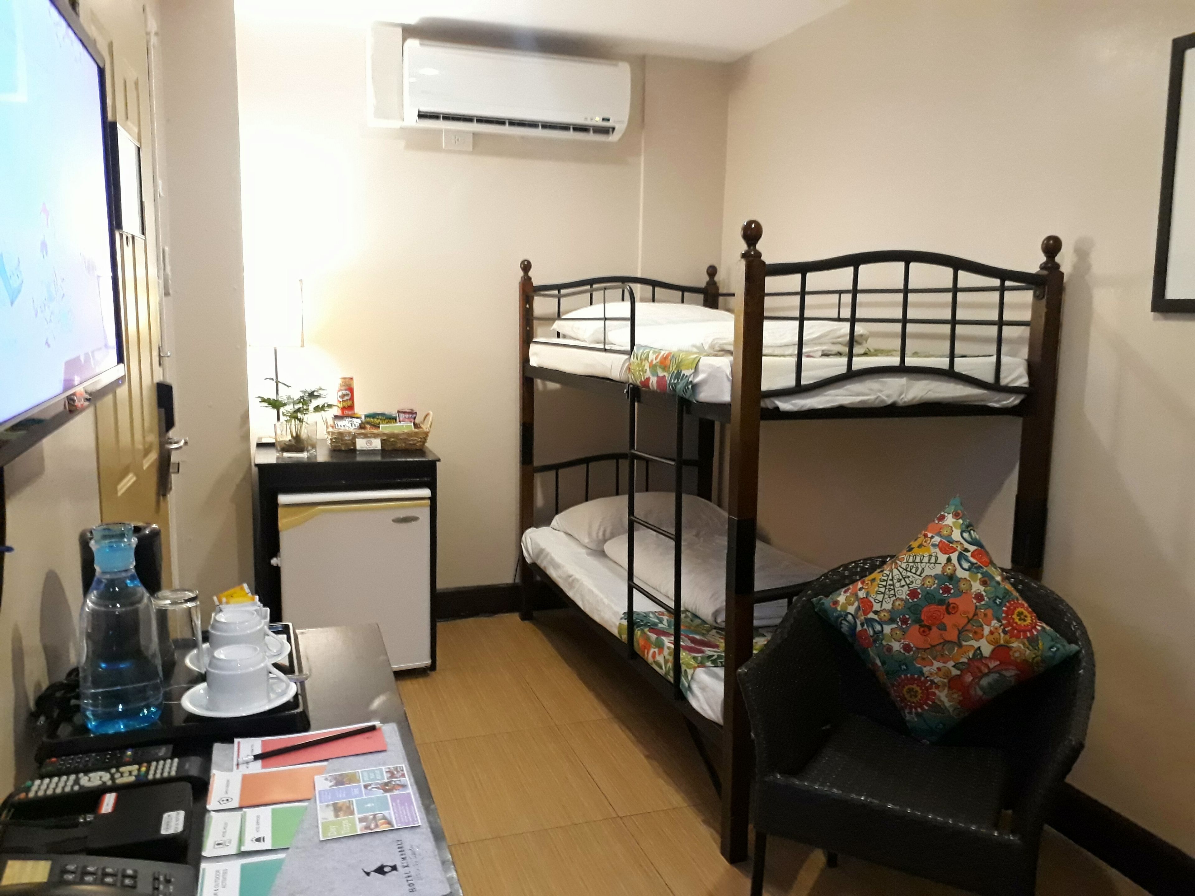 Une chambre de dortoir avec des lits superposés, un bureau avec un ordinateur, un petit réfrigérateur et une chaise avec un coussin coloré.