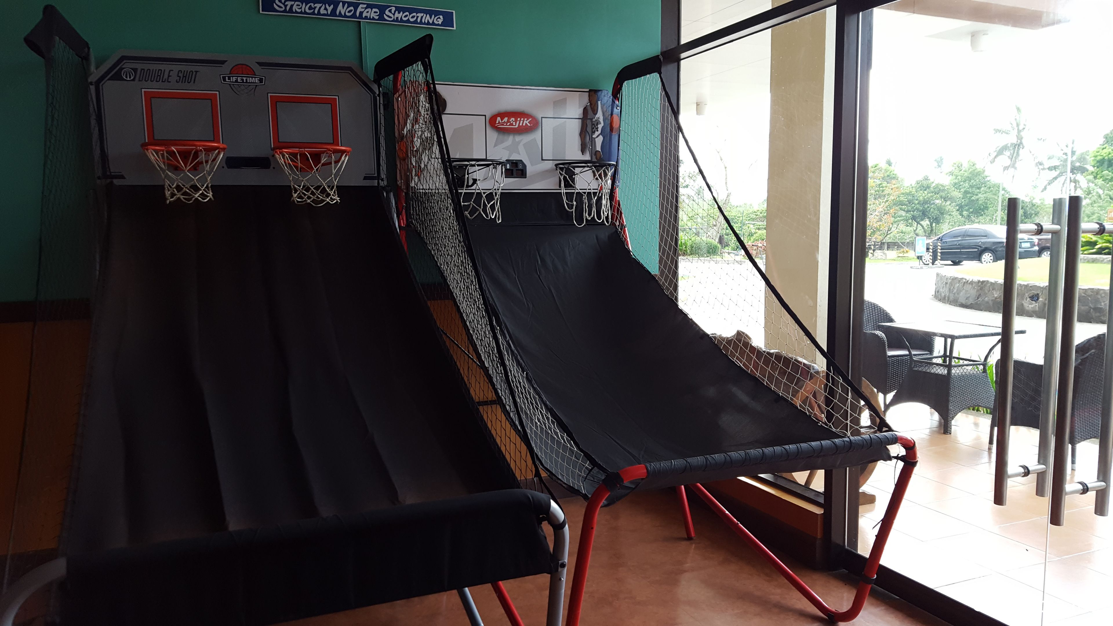 Un terrain de basket avec deux paniers, une zone délimitée par un filet et un panneau indiquant : « Tirs à longue distance strictement interdits ».