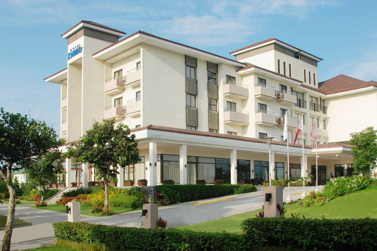 Un hôtel à plusieurs étages, doté d’un design moderne, avec des balcons, de grandes fenêtres et un jardin bien entretenu.