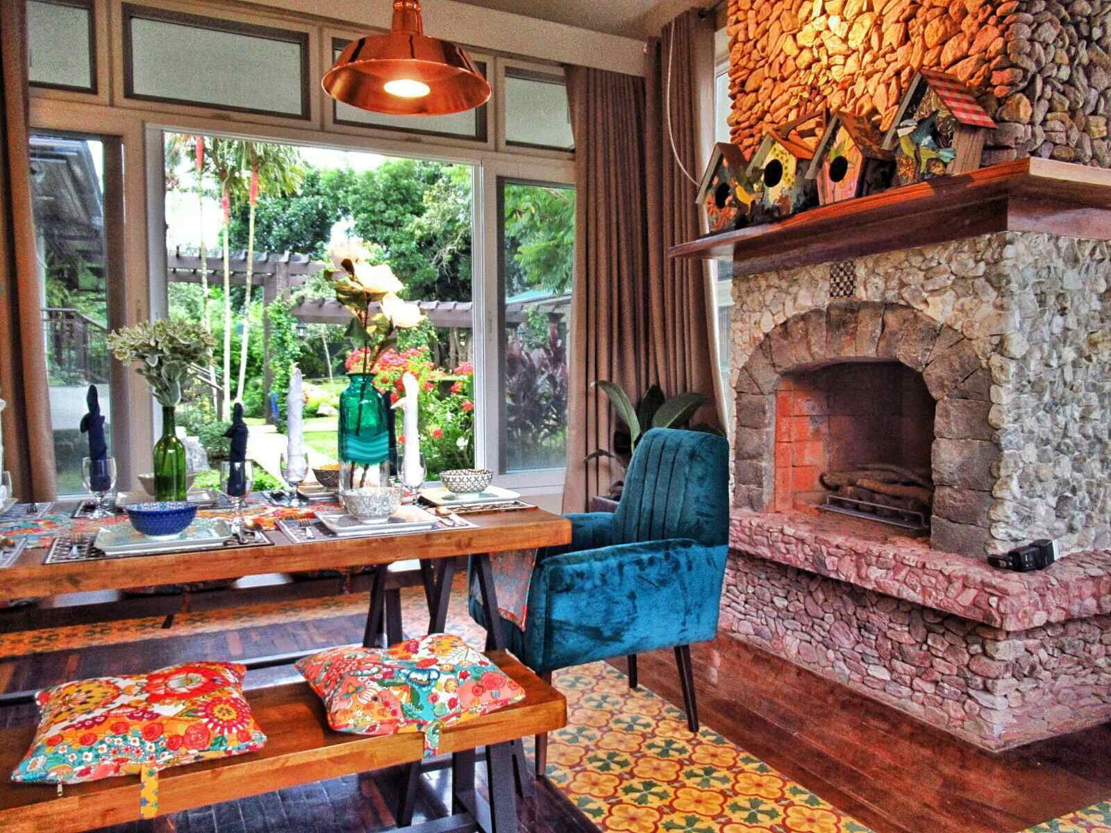 A cozy dining area with a stone fireplace, a table set with dinnerware, and a view of the garden through large windows.
