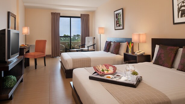A hotel room with two beds, a TV, a chair, a balcony with curtains, and a tray with breakfast items. - Hotel Kimberly Tagaytay (Tagaytay)