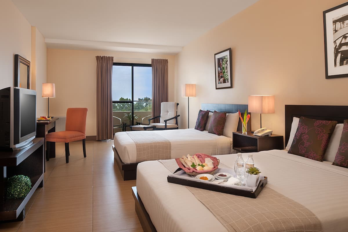 Une chambre d’hôtel avec deux lits, une télévision, une chaise, un balcon avec des rideaux et un plateau contenant des articles pour le petit-déjeuner.