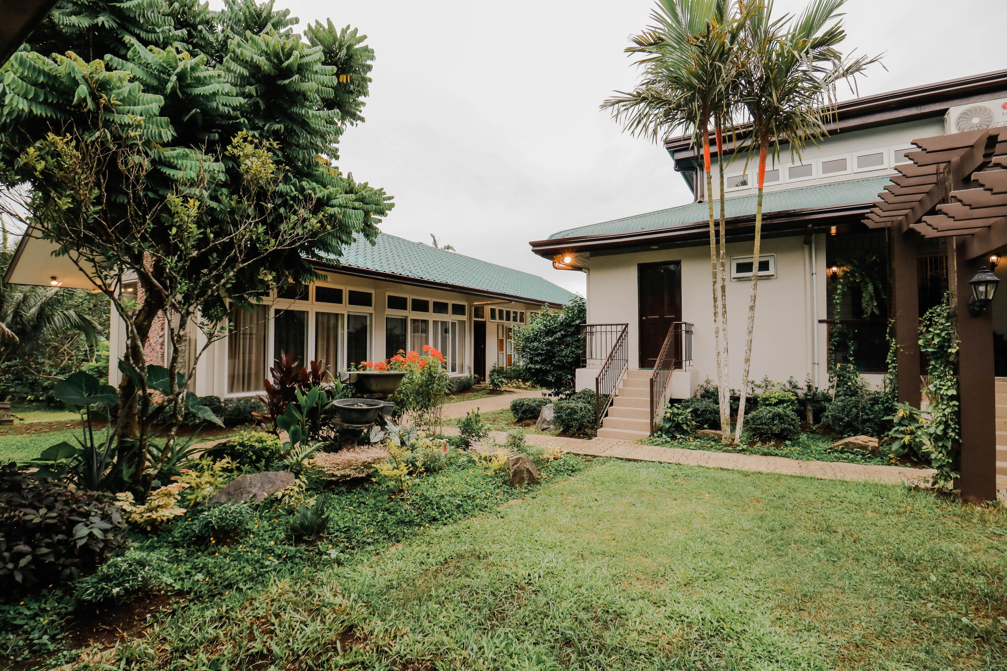 A building with a green roof, surrounded by a well-maintained garden with various plants and a pathway leading to the entrance.