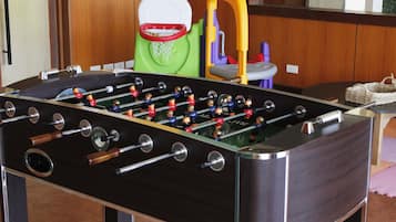 A foosball table with a metal frame and wooden handles, a green and purple chair, and a small table with a woven basket.