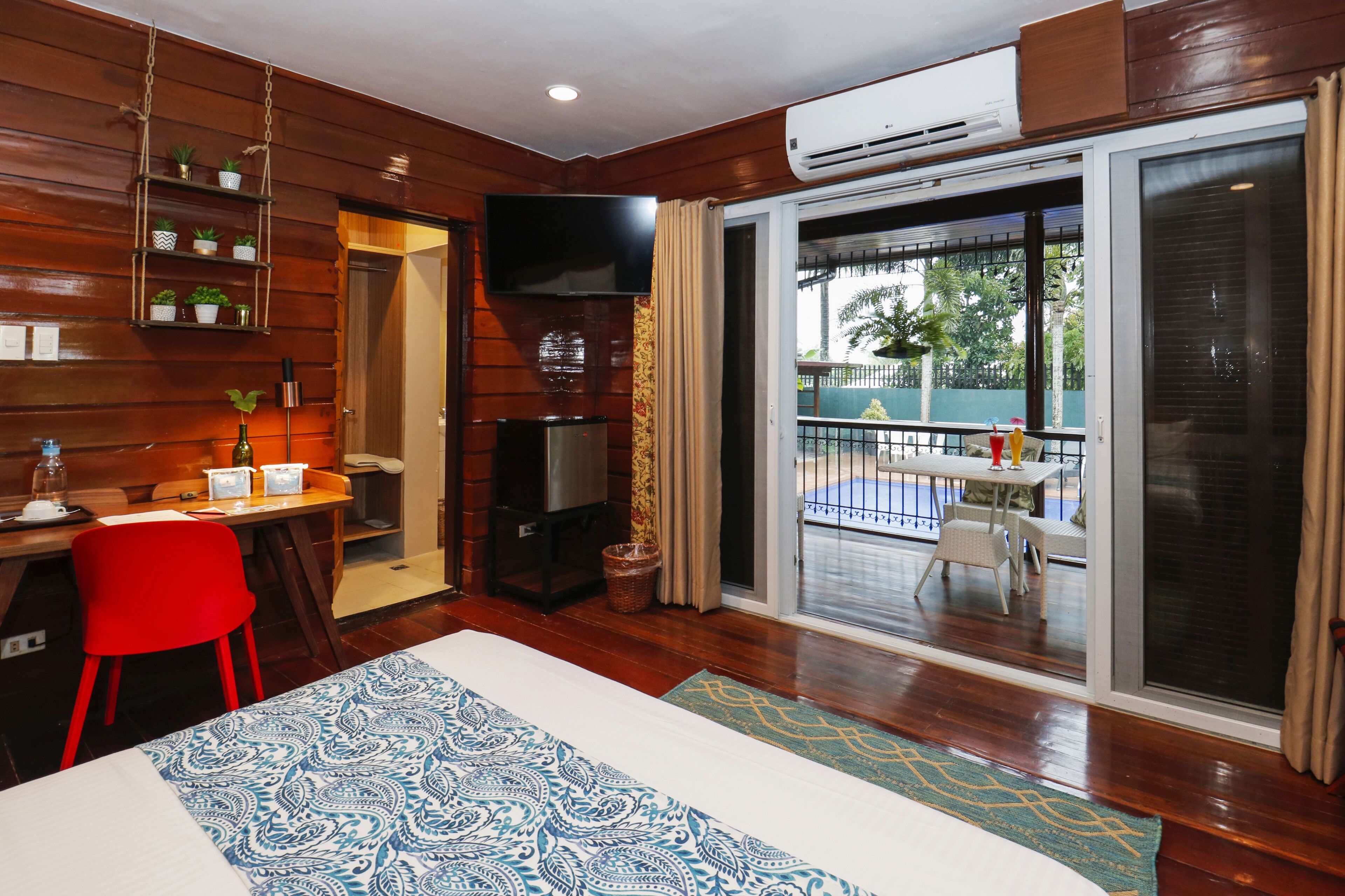 A room with a bed, a desk, a TV, and a balcony with a table and chairs.