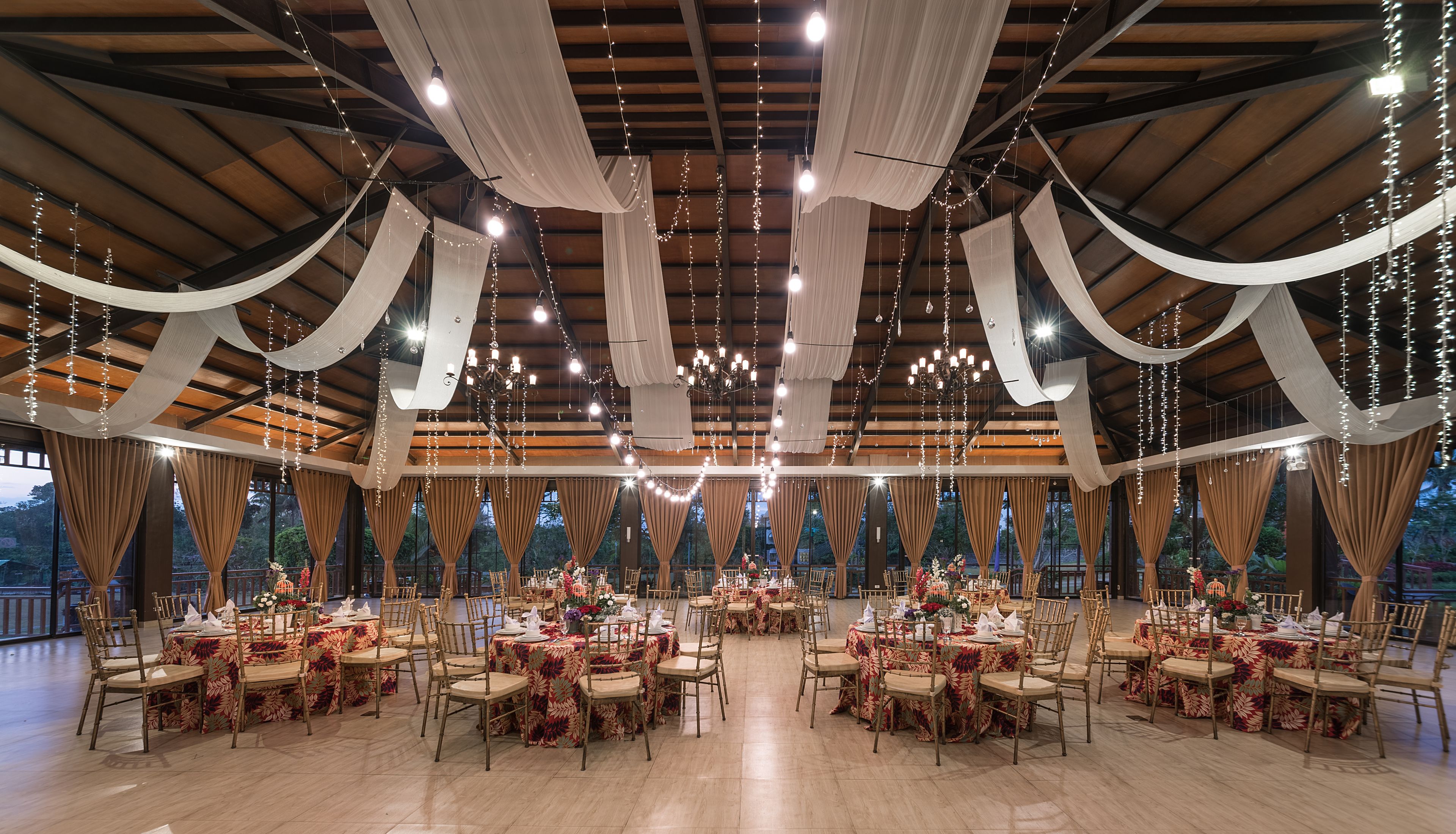 A spacious hall with multiple round tables, draped fabric, and string lights.