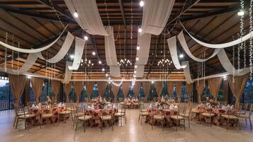 A spacious hall with multiple round tables, draped fabric, and string lights.