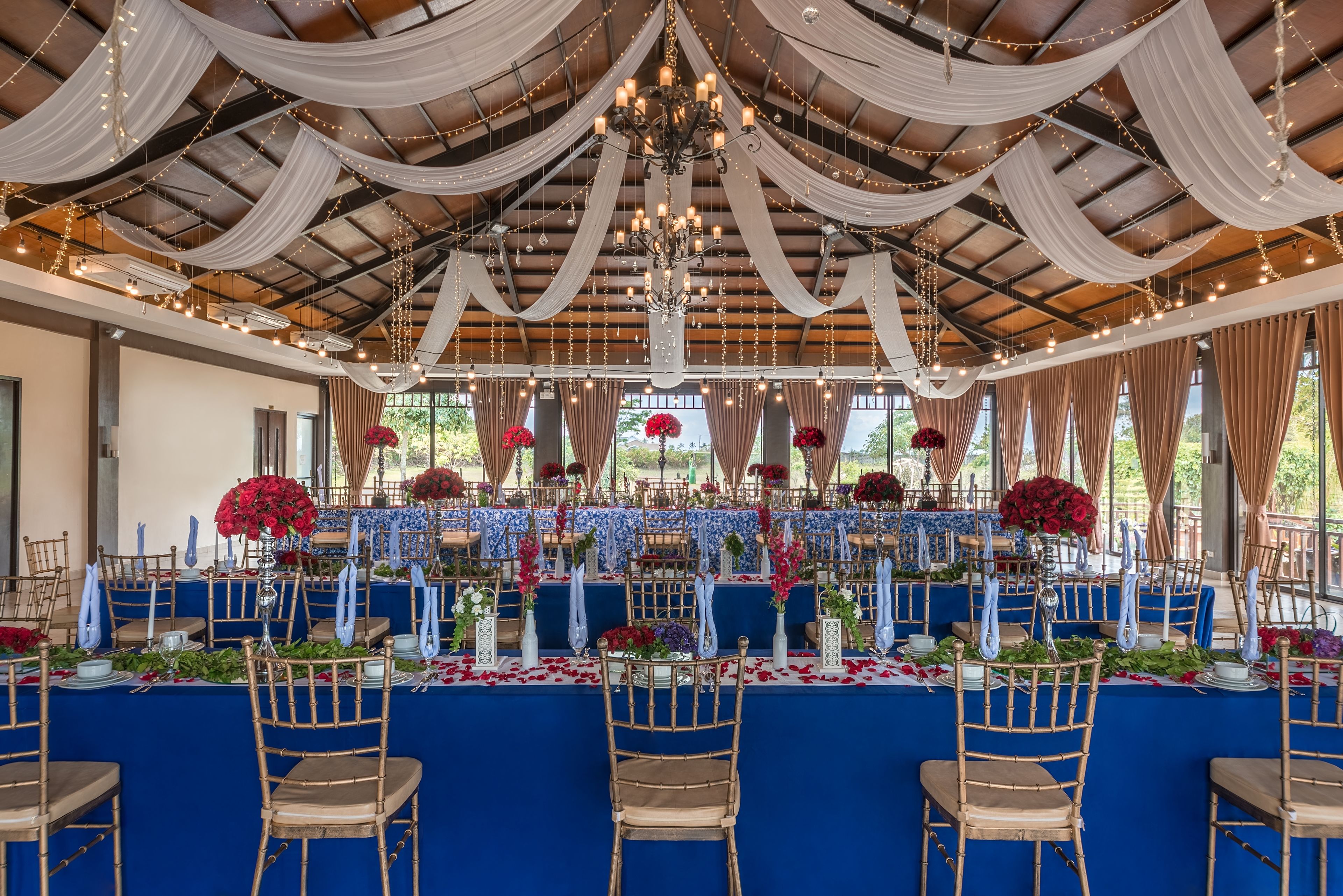 A banquet hall with tables set for a formal event, featuring draped ceilings, chandeliers, and floral centerpieces.