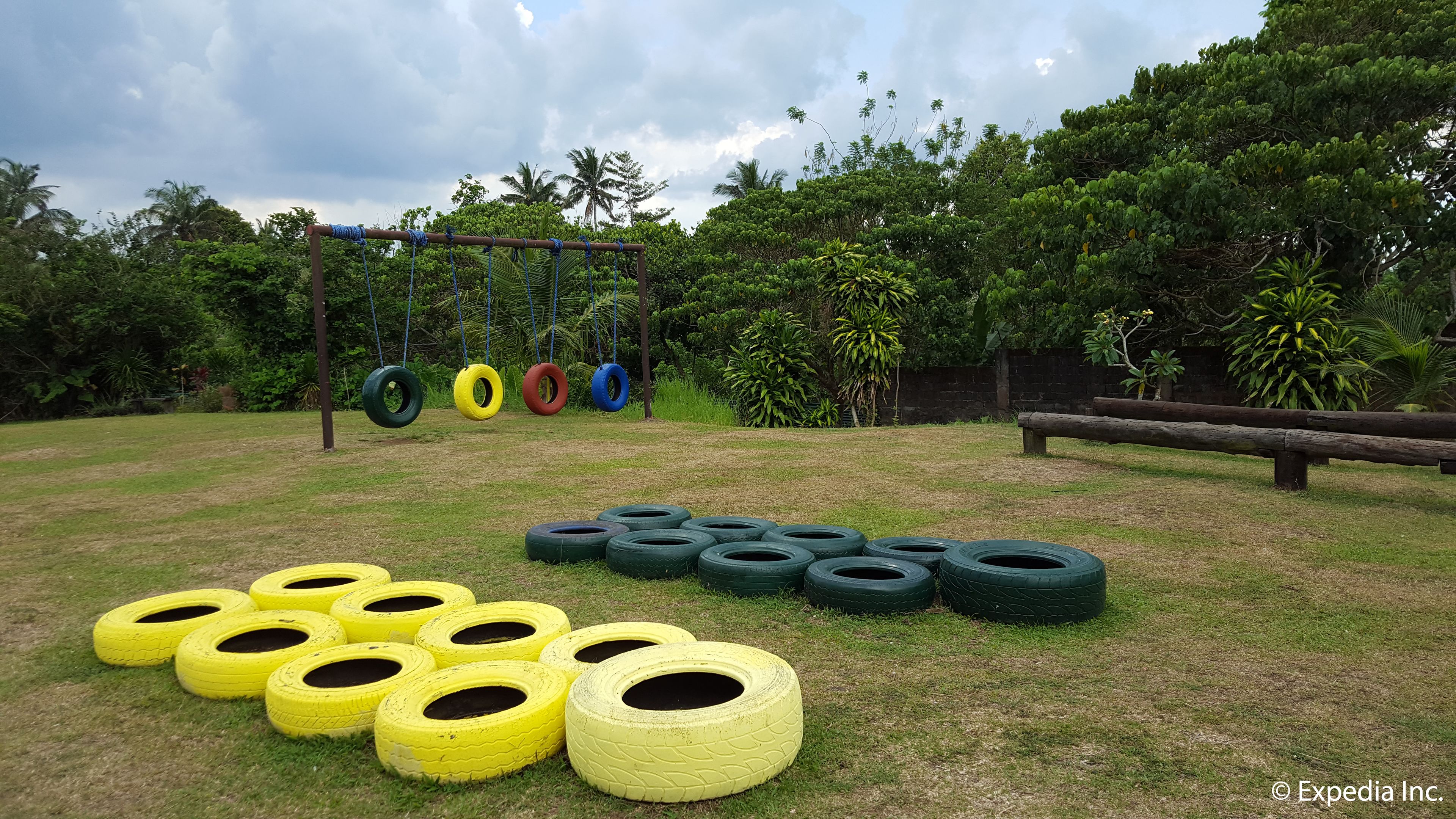 A grassy outdoor area with a tire swing set and a wooden bench.