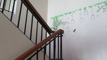 A staircase with wooden handrails and black metal balusters, leading to a landing with a wall decorated with a wall decal of a tree with hanging square boxes and a bird silhouette.
