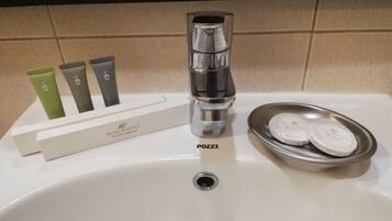 A hotel bathroom sink with a chrome faucet, a soap dish with three bars of soap, and a box of Hotel Kimberly Tooth Care Kit.