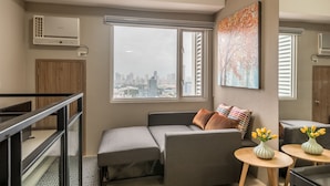 A modern living room with a sofa, a small table with vases, and a city view through a large window. - Hotel Kimberly Manila (Manila)