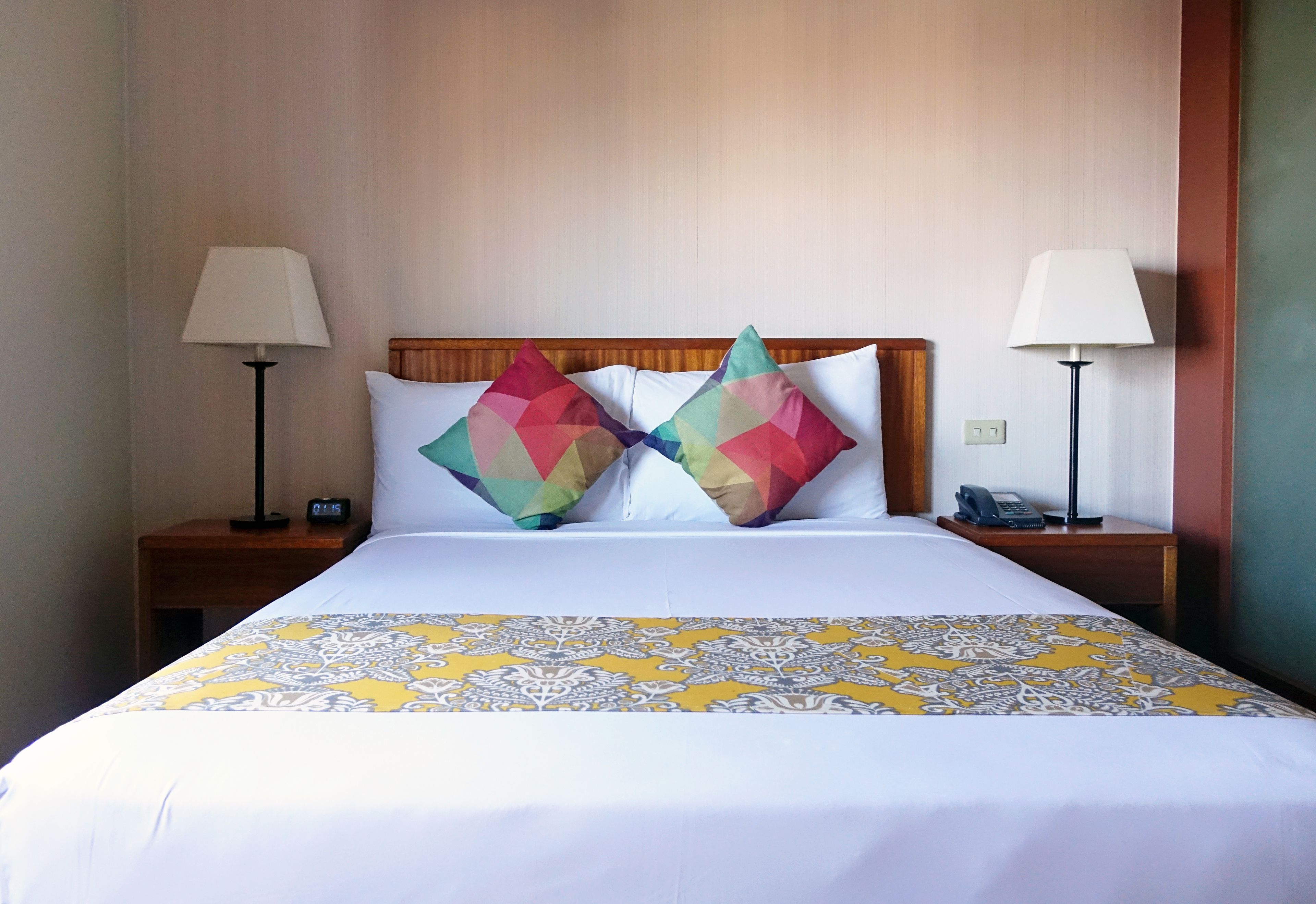 Une chambre d’hôtel avec un lit, deux tables de chevet, une lampe de chaque côté et une couvre-lit à motifs.