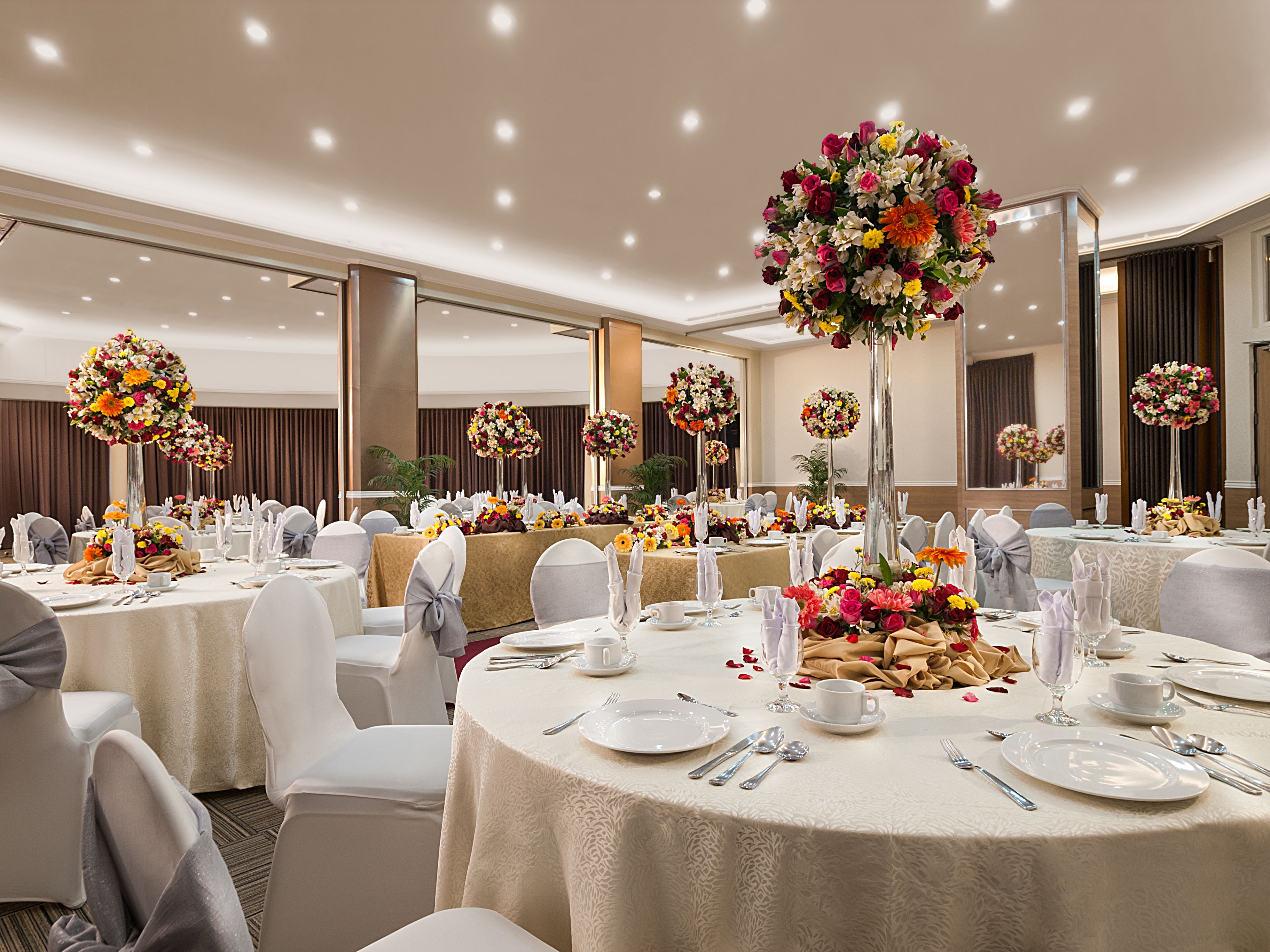 A banquet hall with round tables, white tablecloths, and floral centerpieces.
