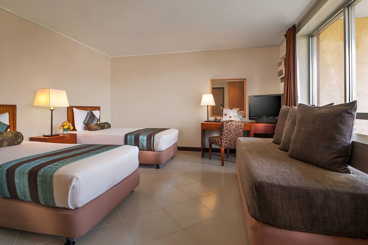 A hotel room with two beds, a desk with a chair, a television, and a large window.
