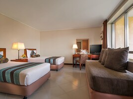 A hotel room with two beds, a desk with a chair, a television, and a large window.