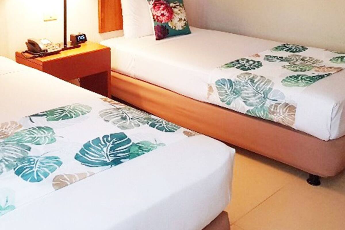 Two single beds with floral bedspreads, a nightstand with a lamp, and a telephone.