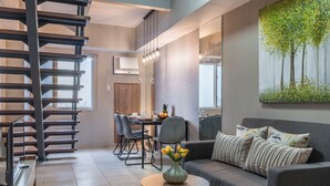 A modern living room with a grey sofa, a dining area with a table and chairs, a staircase, and a large painting of trees. - Hotel Kimberly Manila (Manila)