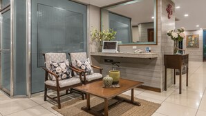 A modern bathroom with a glass shower enclosure, two upholstered chairs, a wooden table, and a mirror above a vanity. - Hotel Kimberly Manila (Manila)