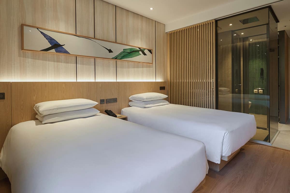 A hotel room with two beds, a large window, and a modern design.