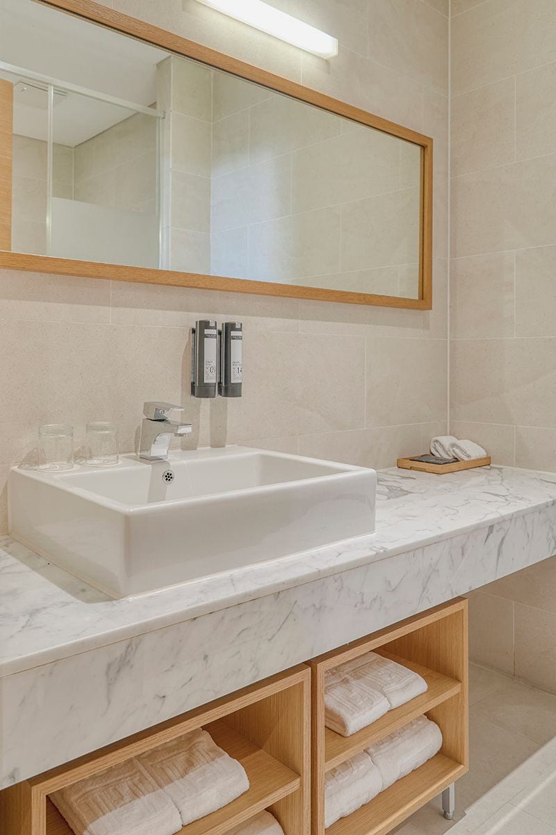 A bathroom with a white sink, a mirror, and a wooden shelf with towels.