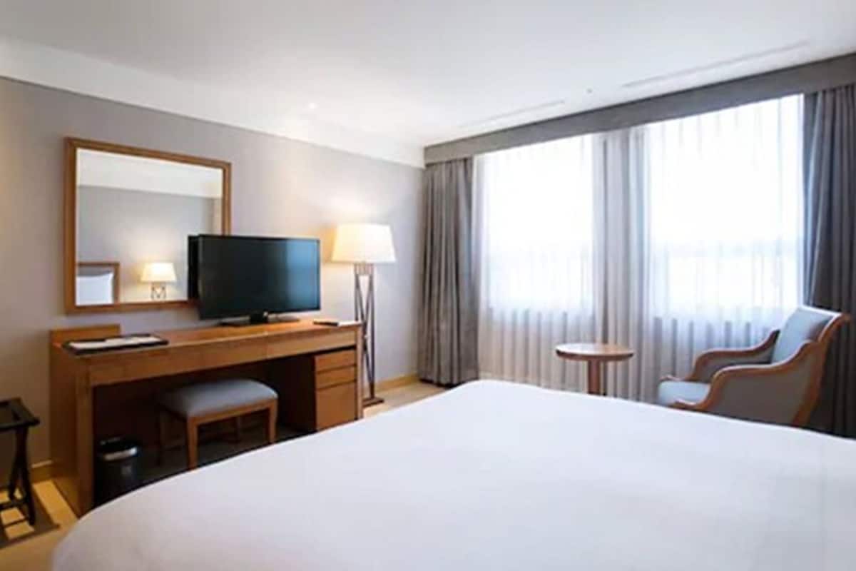 A hotel room with a large bed, a desk with a television, a chair, and a small table.