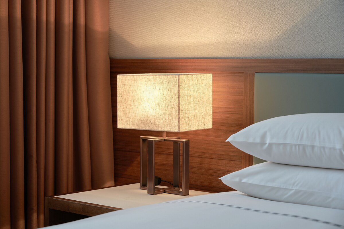 Una cama bien hecha con almohadas blancas y una mesita de noche con lámpara.