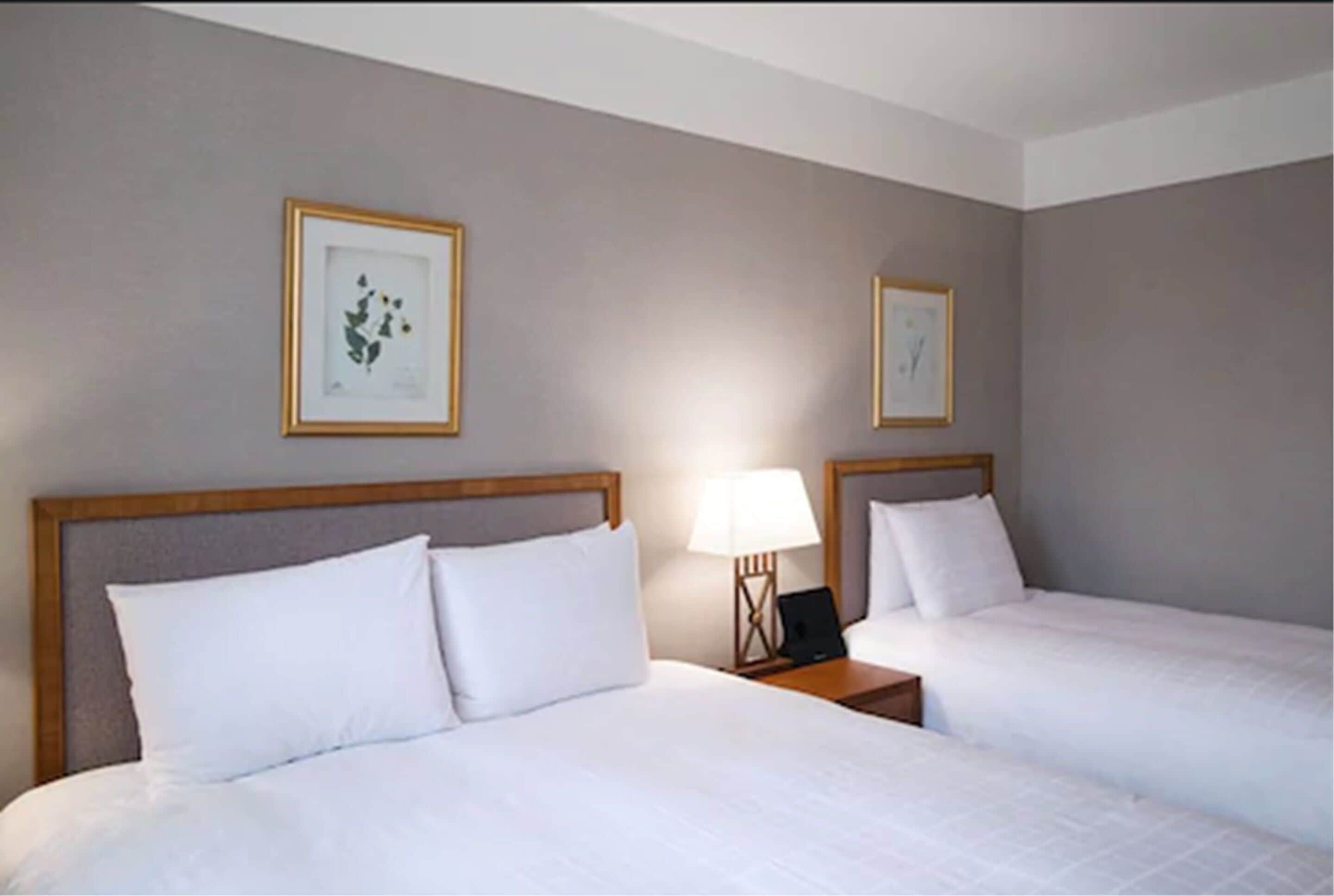 Habitación de hotel con dos camas, una mesita de noche con lámpara y cuadros en la pared.