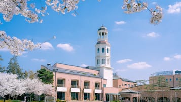 A building with a central tower, surrounded by a garden with blooming trees.
