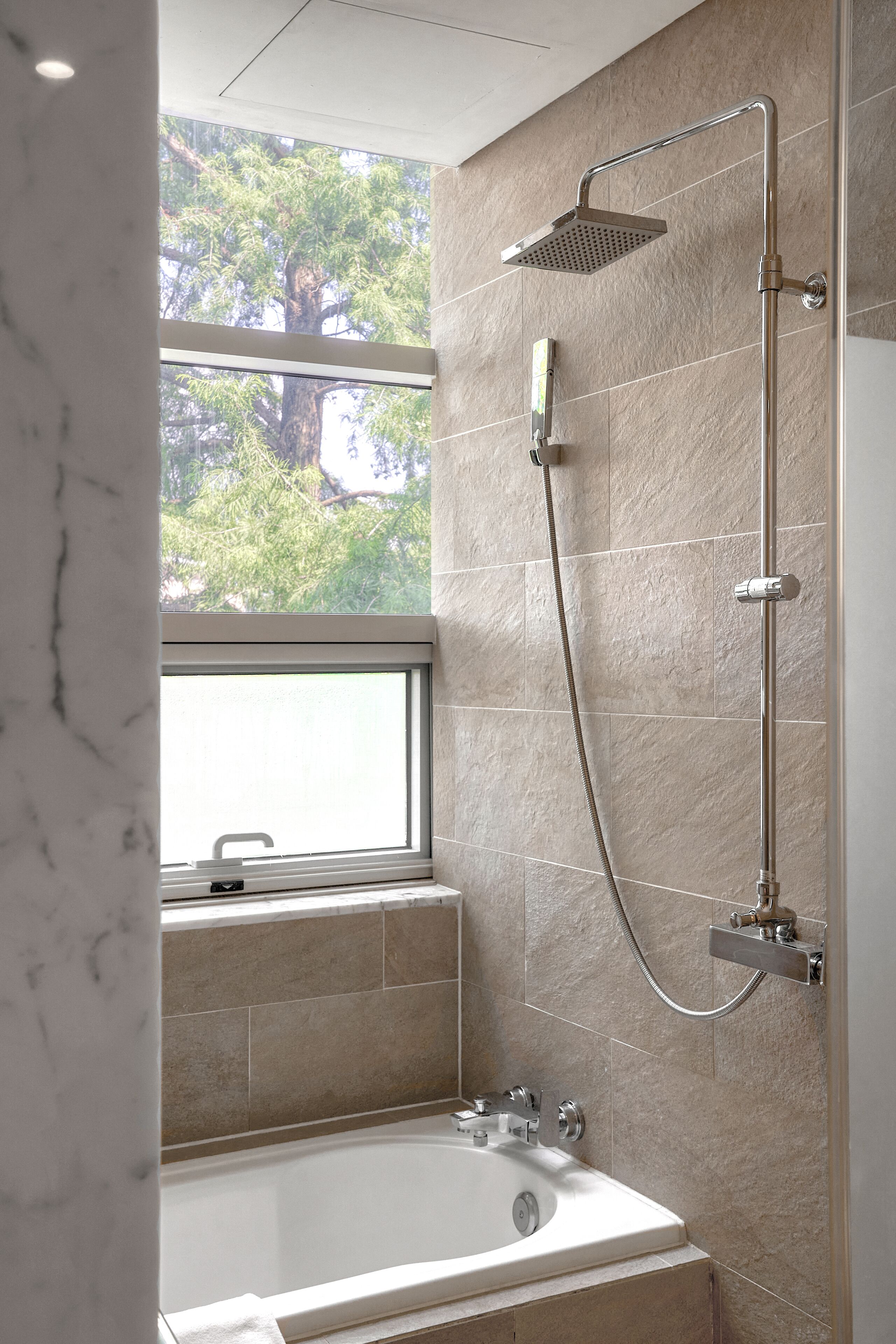 Une salle de bain moderne avec une baignoire, une douche à pommeau de pluie et une fenêtre donnant sur les arbres.