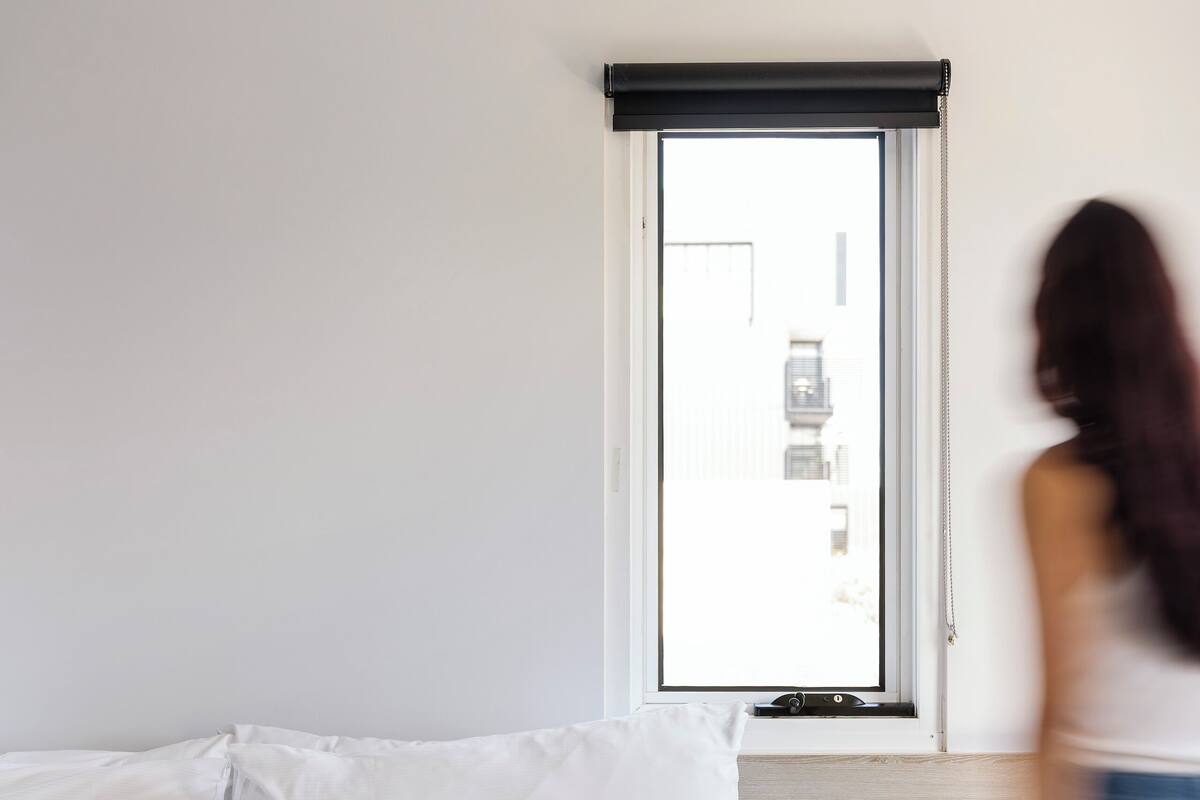 A hotel room with a bed, a window with a view, and a bedside table with a cup and book.