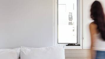 Quarto de hotel com cama, janela e vista, e mesa de cabeceira com uma chávena e um livro.