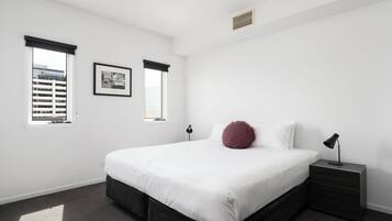 A bedroom with a bed, bedside table, lamp, window, and picture on the wall.
