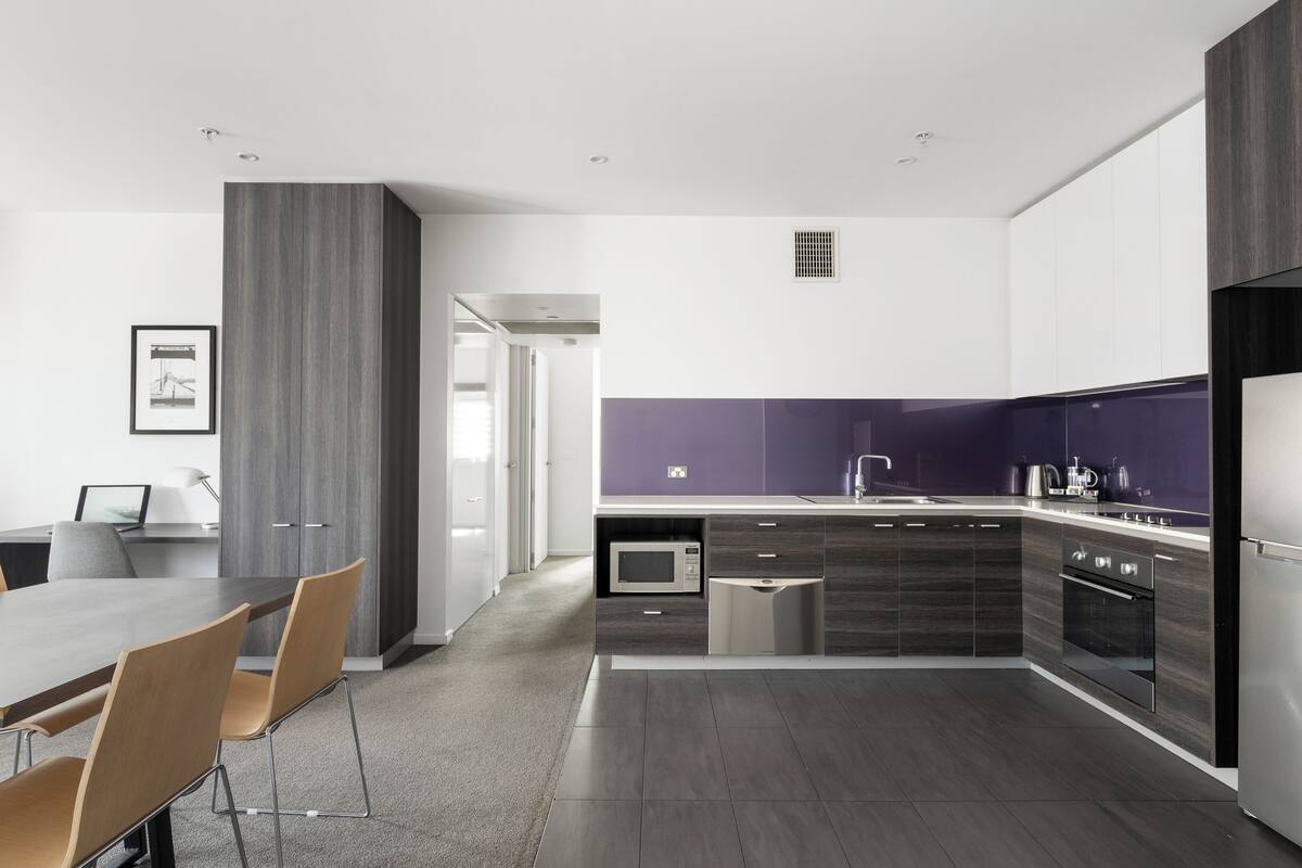 A modern kitchen with dark cabinetry, a built-in microwave, and a stainless steel refrigerator.