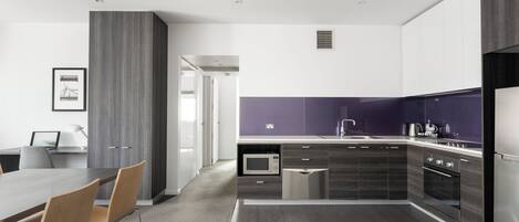 A modern kitchen with dark cabinetry, a built-in microwave, and a stainless steel refrigerator.