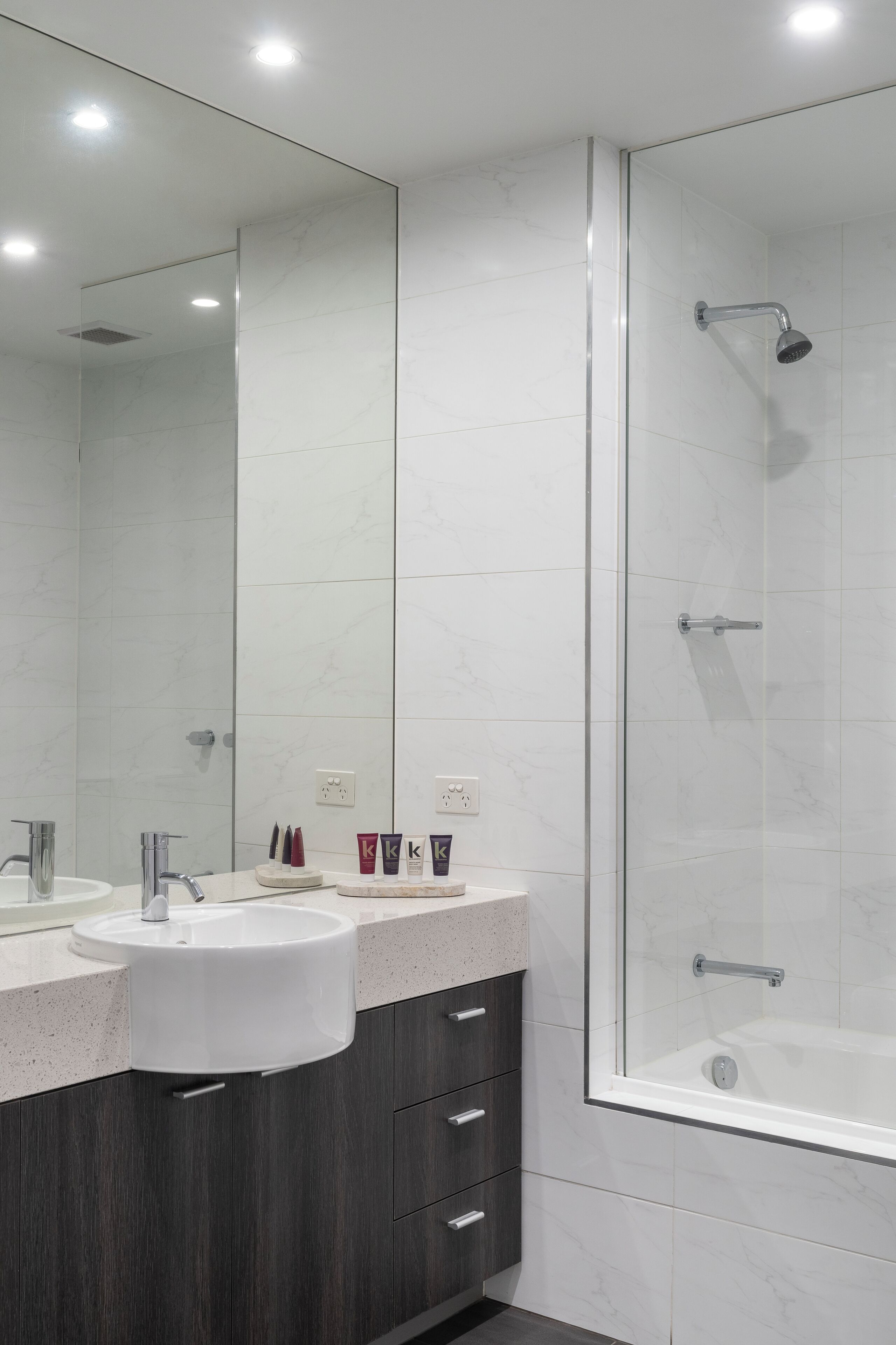 A modern bathroom with a glass-enclosed shower, a double sink vanity, and marble tiles.