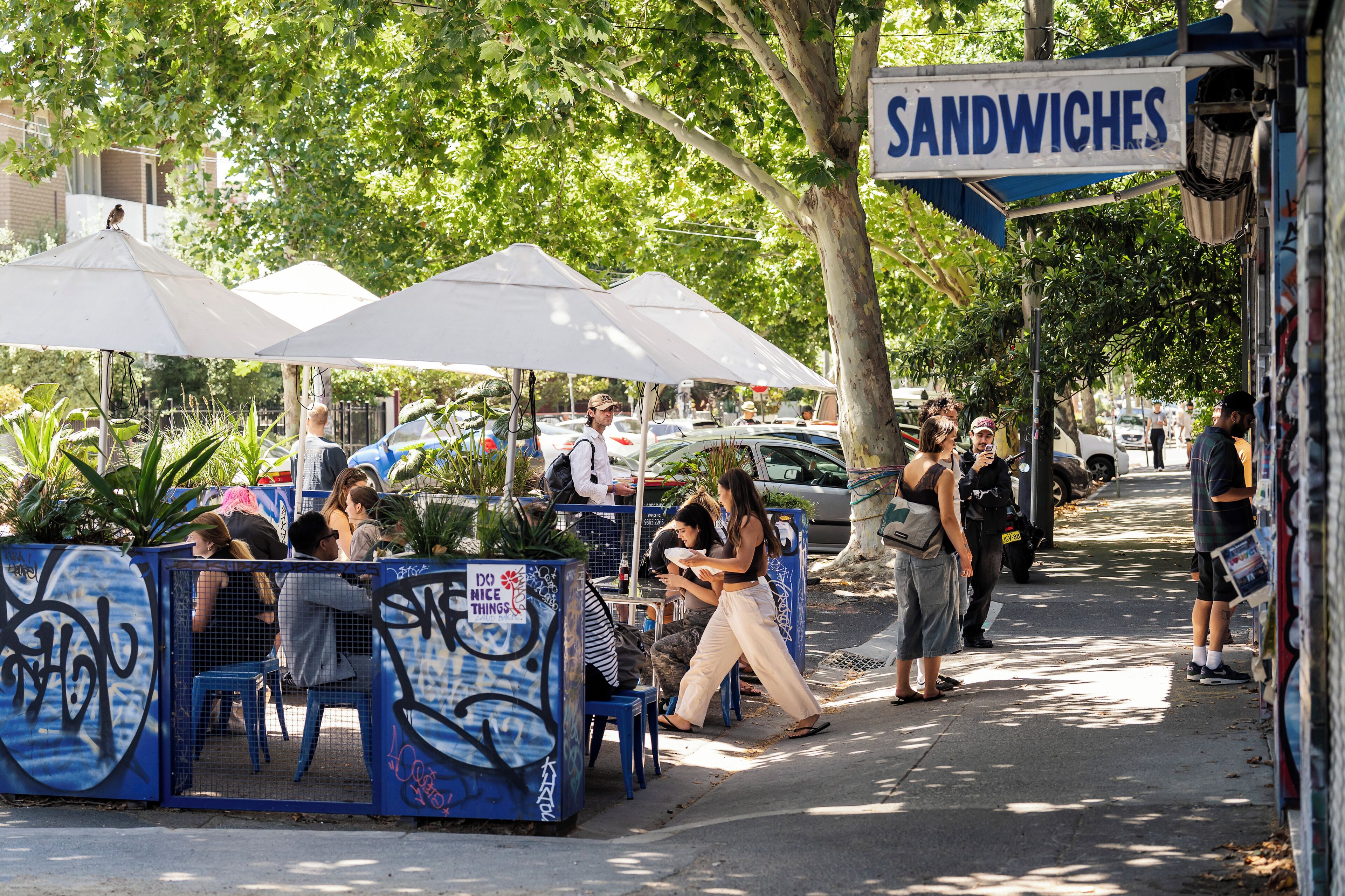 Ein Straßencafé mit Außenbestuhlung, einem Sandwichangebot und einer von Bäumen gesäumten Straße.