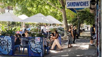 Ein Straßencafé mit Außenbestuhlung, einem Sandwichangebot und einer von Bäumen gesäumten Straße.