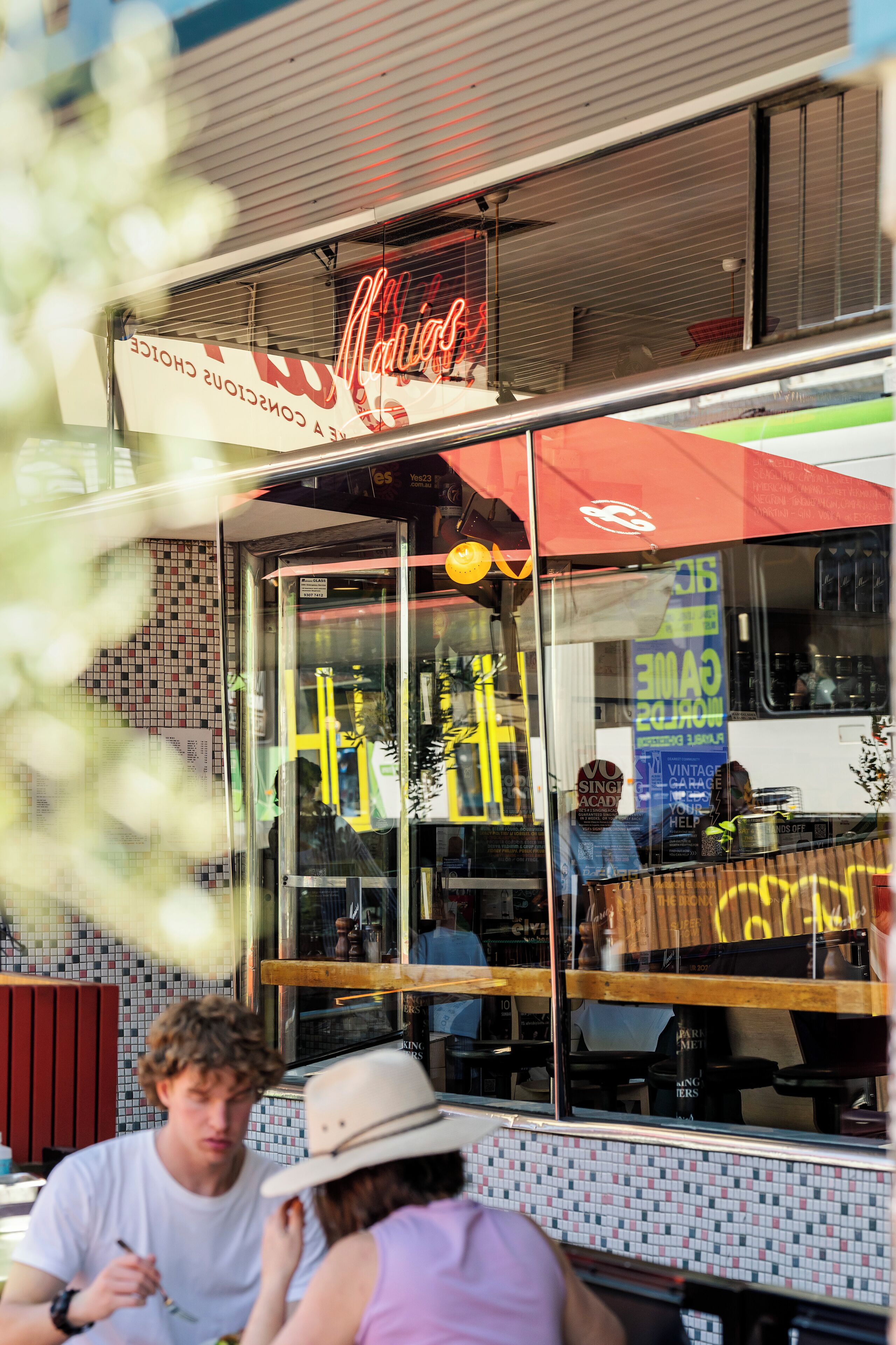 A restaurant with a neon sign, a tiled wall, and a window reflecting interior seating.