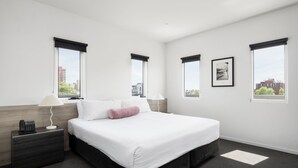 Una habitación de hotel moderna con una cama grande, una mesita de noche con lámpara y vistas a la ciudad a través de las ventanas.