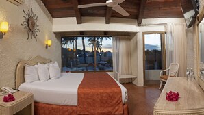 Ein Hotelzimmer mit Bett, Tisch, Stuhl, einem Balkon mit Blick und einem Deckenventilator.