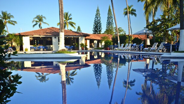 Ein Pool mit klarem Wasser, das Palmen und ein Gebäude mit einem Ziegeldach reflektiert.