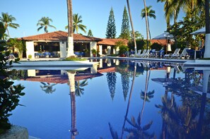 Una piscina de aguas cristalinas que refleja palmeras y un edificio con techo de tejas.
