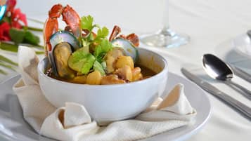 A bowl of seafood stew with a crab, mussels, and cilantro, served on a white plate with a napkin.