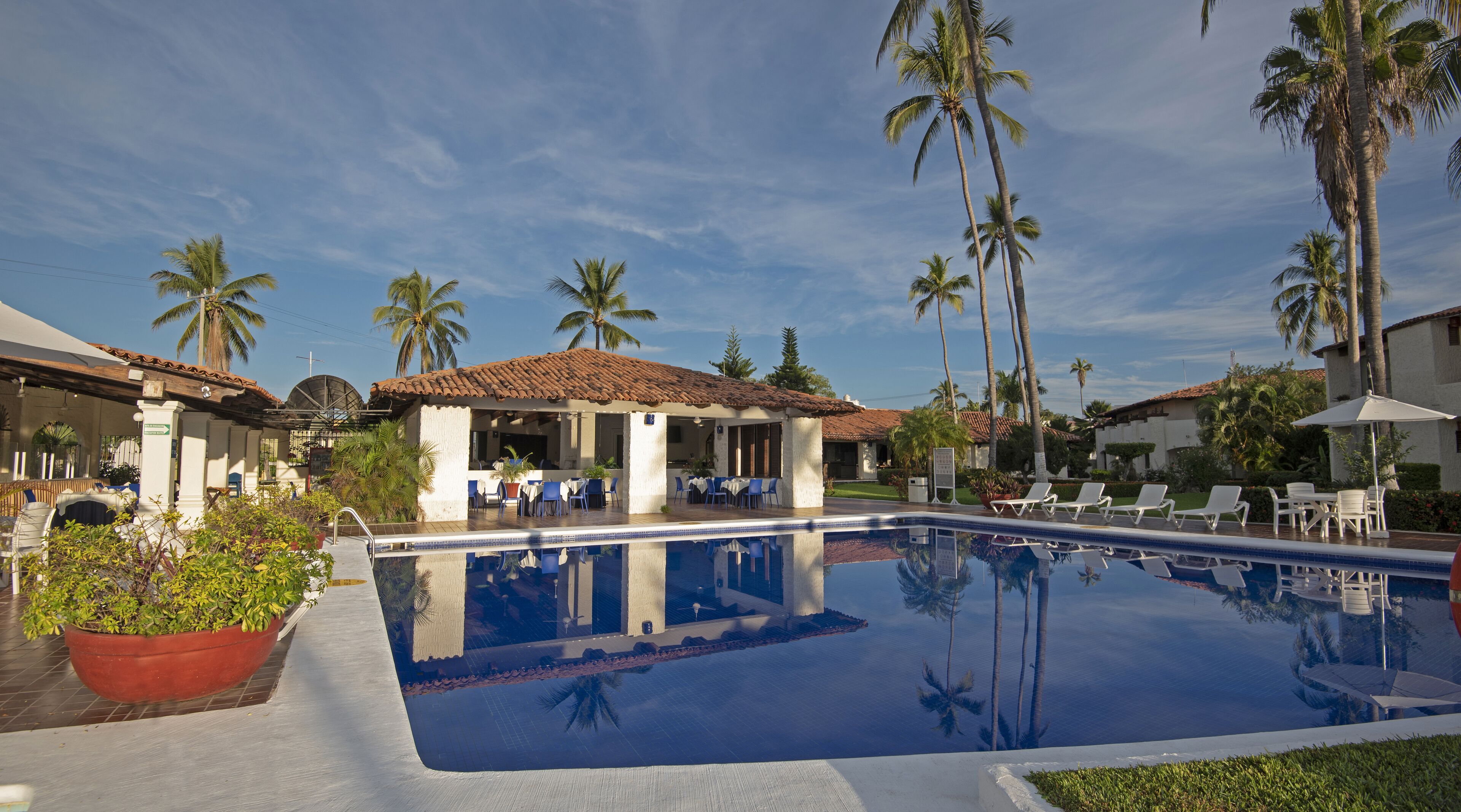 A pool area with lounge chairs and a covered seating area, surrounded by palm trees.