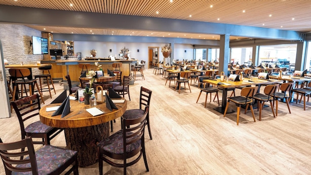 A spacious restaurant with wooden tables and chairs, a bar area, and large windows allowing natural light. - Hotel Pejsegården (Braedstrup)