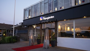 A hotel reception with a modern glass facade, a red carpet, and potted plants. - Hotel Pejsegården (Braedstrup)